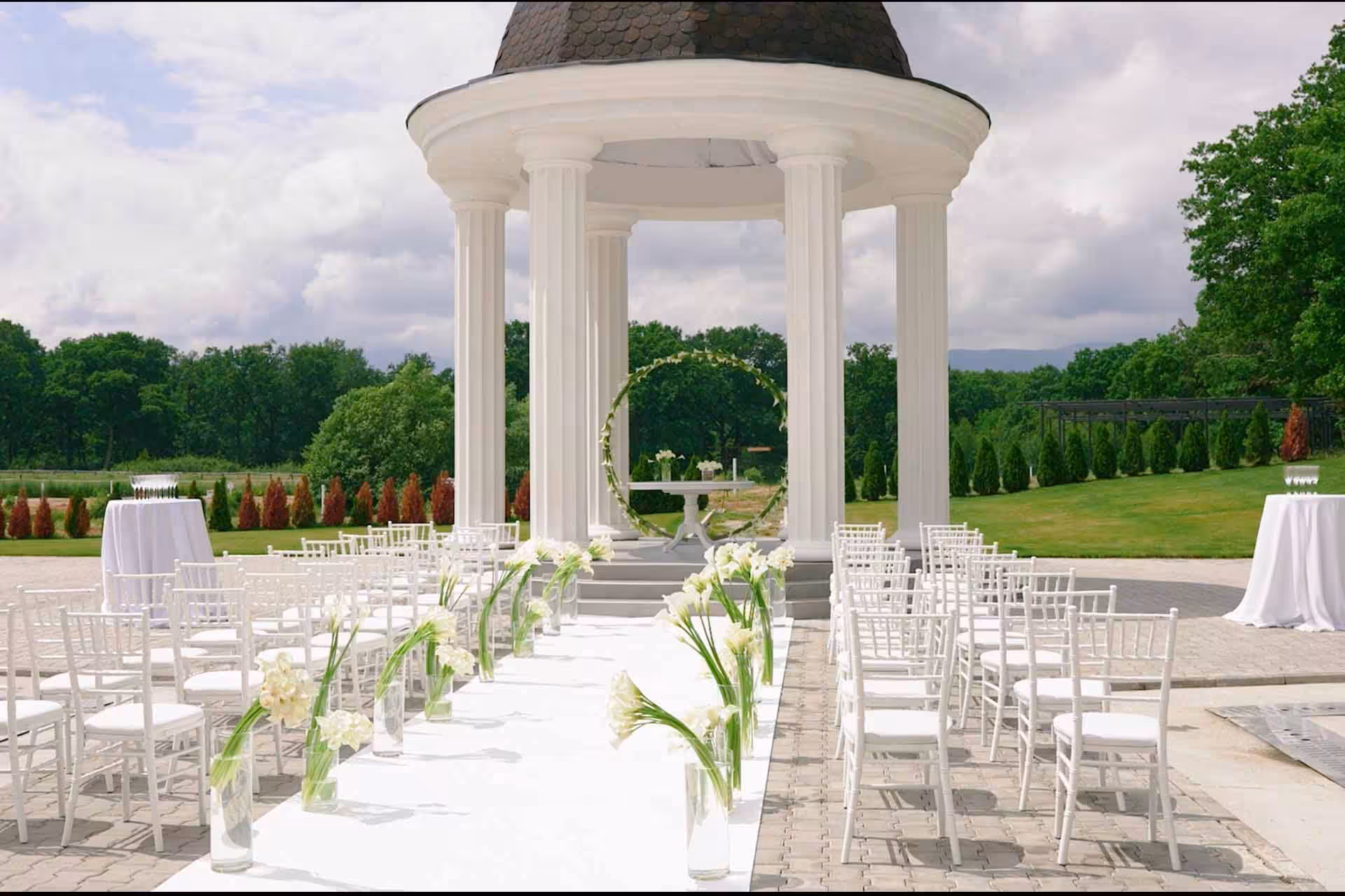 Fotograf nuntă Sibiu – Cupola de ceremonii alb-crem cu scaune cu perne bej, aranjament floral de caliță în frunze verzi, locație de nuntă perfectă cu peluză naturală